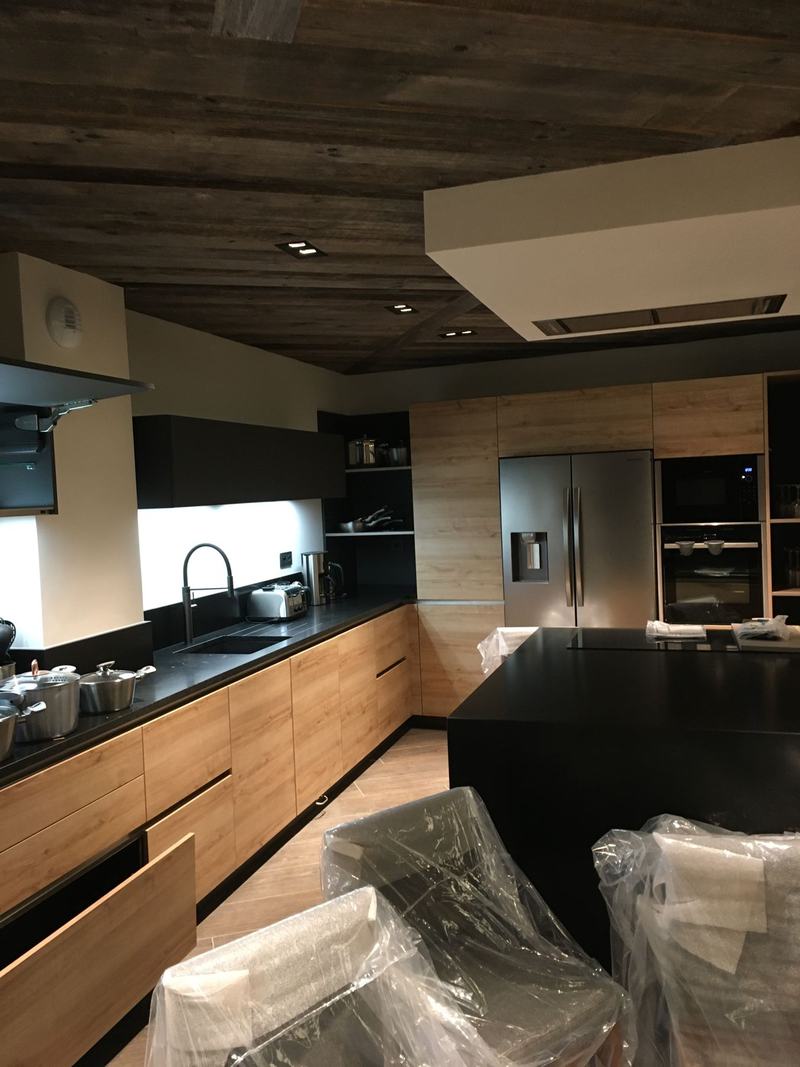 Cuisine aux façades bois et plan noir sous un plafond en vieux bois